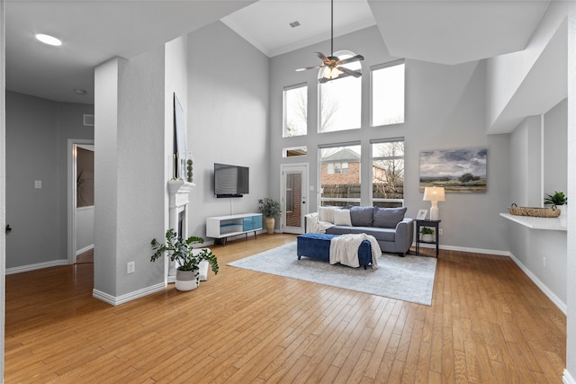 living room with a towering ceiling, light hardwood / wood-style flooring, ornamental molding, and ceiling fan