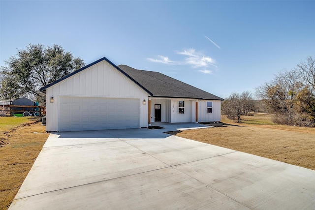 modern farmhouse featuring a shingled roof, concrete driveway, an attached garage, a front lawn, and board and batten siding