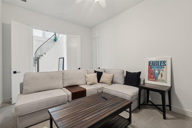 living room featuring light colored carpet, ceiling fan, stairway, and baseboards