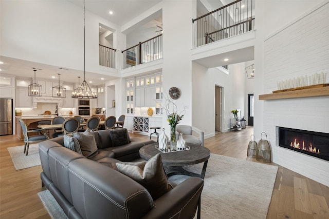 living area with light wood finished floors, a high ceiling, a large fireplace, baseboards, and ceiling fan with notable chandelier