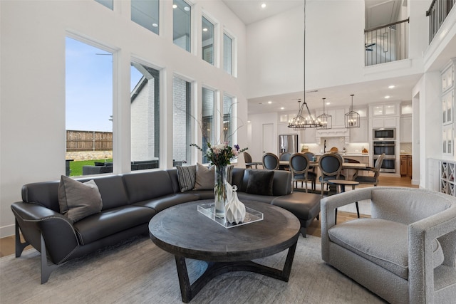 living room featuring recessed lighting, an inviting chandelier, a high ceiling, and light wood-style flooring
