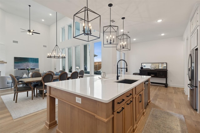 kitchen featuring decorative light fixtures, sink, white cabinets, stainless steel fridge, and a center island with sink