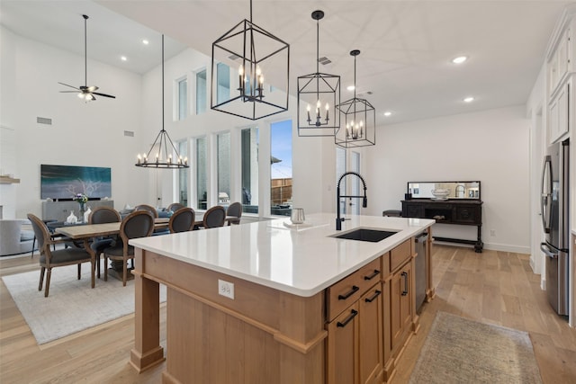 kitchen featuring an island with sink, appliances with stainless steel finishes, a sink, light wood-type flooring, and open floor plan