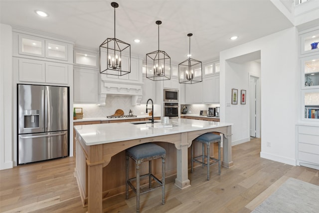 kitchen with white cabinetry, stainless steel appliances, an island with sink, decorative backsplash, and decorative light fixtures