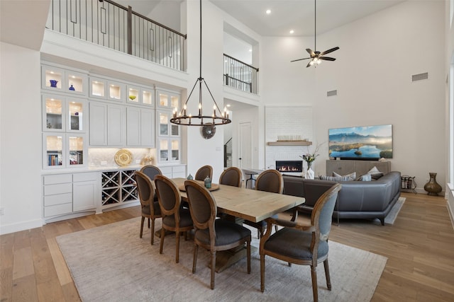 dining room with visible vents, ceiling fan with notable chandelier, light wood-style floors, and a brick fireplace