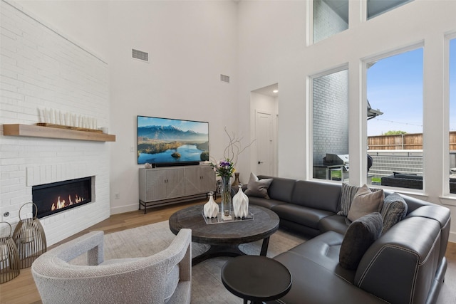 living area featuring wood finished floors, visible vents, a high ceiling, and a brick fireplace