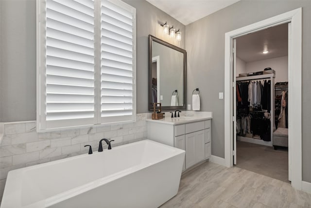 full bath with vanity, a walk in closet, and a soaking tub