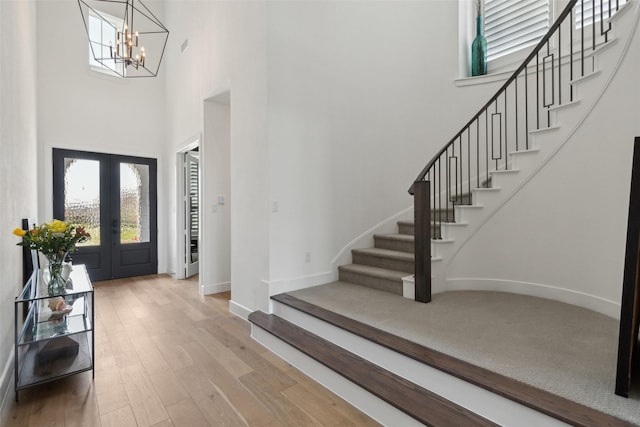 foyer with a high ceiling, wood-type flooring, an inviting chandelier, and french doors