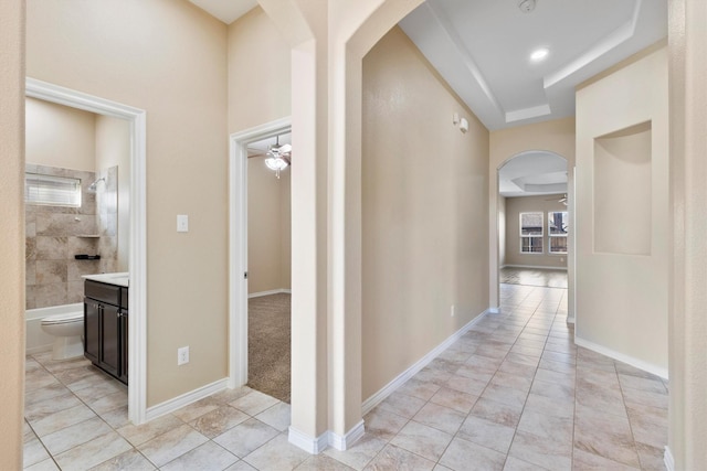 hall with arched walkways, light tile patterned floors, and baseboards