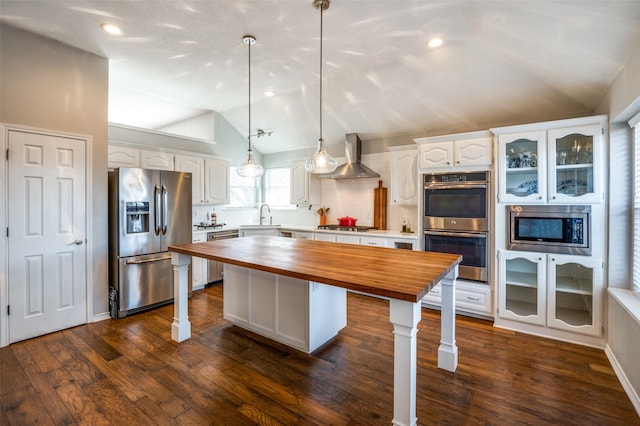 kitchen featuring sink, white cabinets, hanging light fixtures, stainless steel appliances, and wall chimney exhaust hood