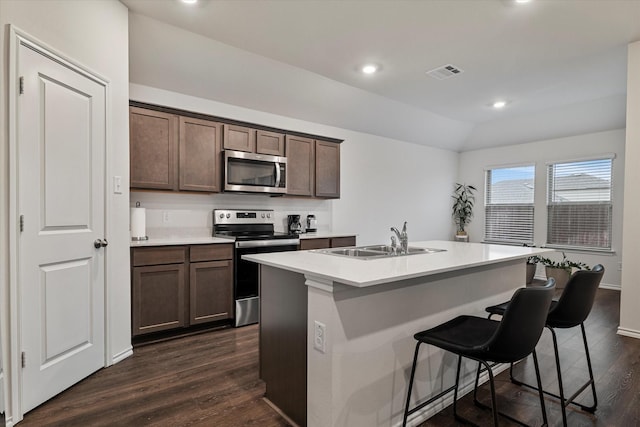 kitchen with sink, appliances with stainless steel finishes, dark hardwood / wood-style floors, dark brown cabinetry, and a center island with sink