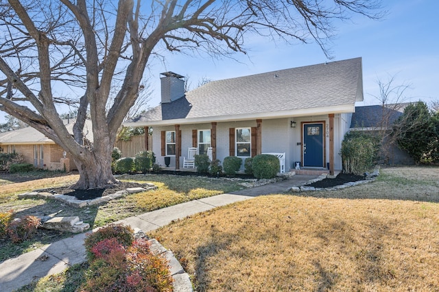 view of front facade with brick siding, a chimney, a front yard, and a shingled roof