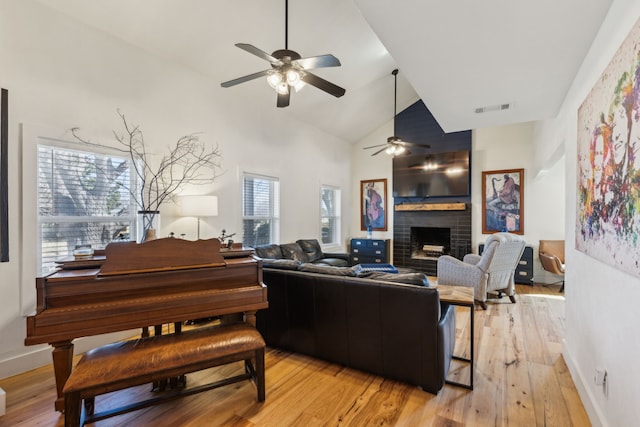 living area with light wood-style floors, visible vents, a fireplace, and high vaulted ceiling