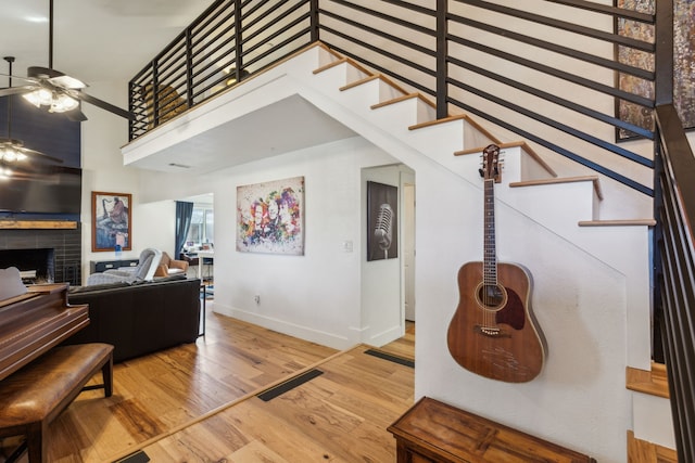 living area featuring a fireplace, wood finished floors, a towering ceiling, visible vents, and a ceiling fan