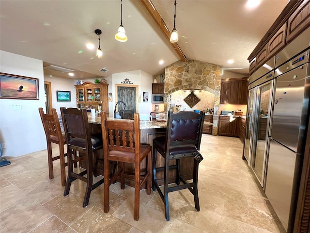 kitchen with a large island, vaulted ceiling with beams, hanging light fixtures, built in appliances, and light stone countertops