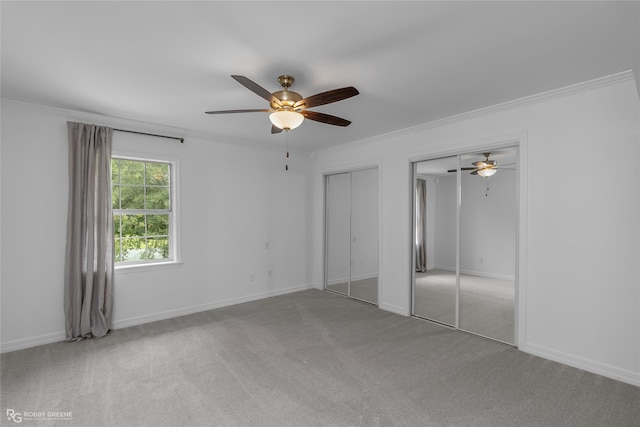 unfurnished bedroom with light colored carpet, ornamental molding, and two closets