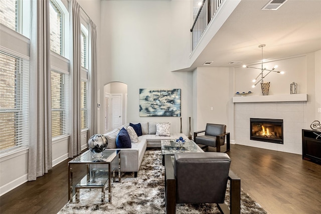 living room featuring dark wood-type flooring, a towering ceiling, an inviting chandelier, and a tile fireplace