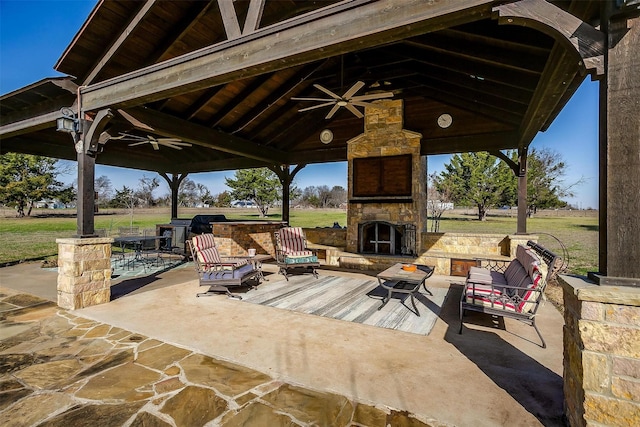 view of patio / terrace with area for grilling, an outdoor living space with a fireplace, a gazebo, and ceiling fan