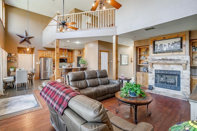 living room with wood-type flooring, a stone fireplace, built in features, and ceiling fan