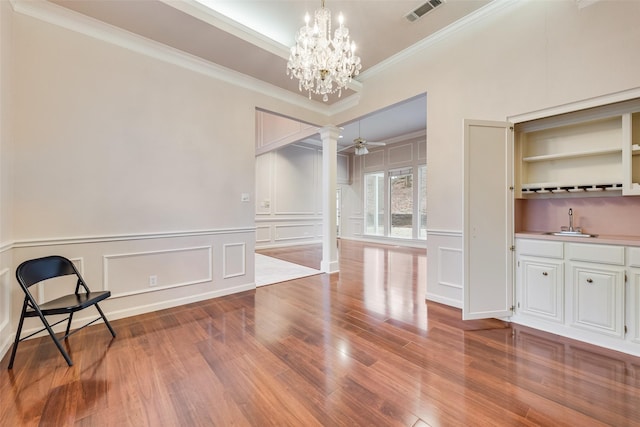 dining space featuring sink, hardwood / wood-style flooring, ornamental molding, ceiling fan with notable chandelier, and ornate columns