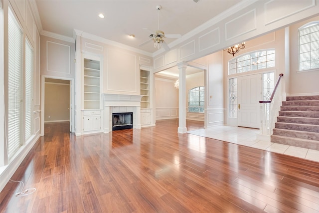 unfurnished living room featuring ornate columns, built in features, a fireplace, crown molding, and light wood-type flooring