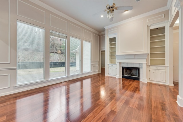 unfurnished living room featuring a tile fireplace, ornamental molding, wood-type flooring, and built in shelves