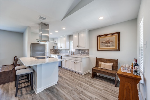 kitchen with stainless steel appliances, island range hood, light stone countertops, and white cabinets