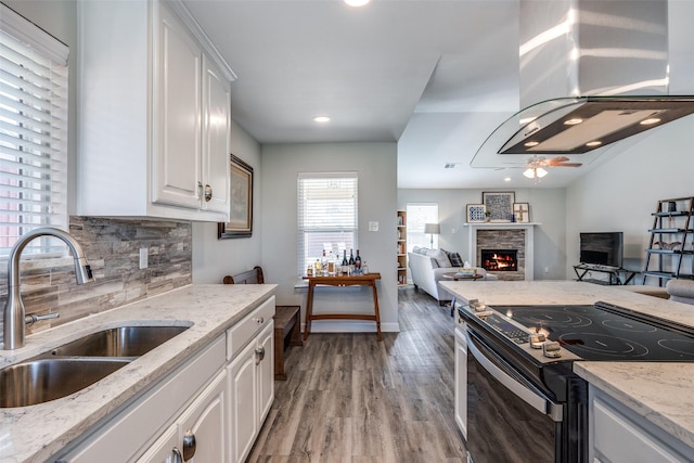 kitchen with electric stove, open floor plan, white cabinetry, a sink, and a stone fireplace