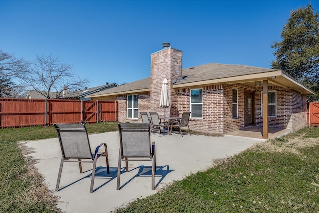 back of property with a patio area, a fenced backyard, brick siding, and a chimney