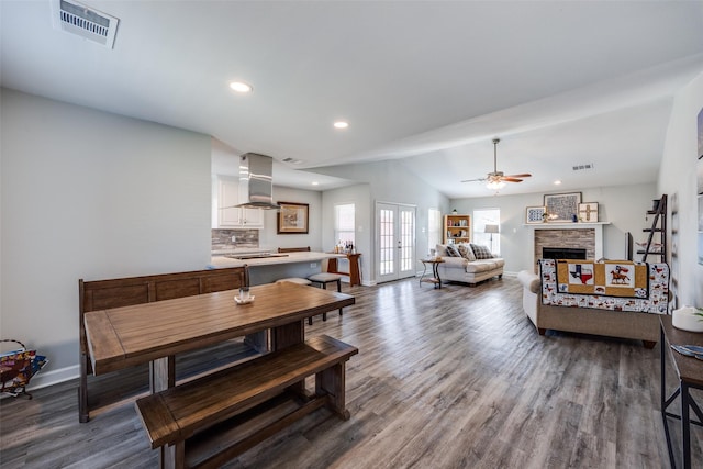 dining room featuring lofted ceiling, a fireplace, wood finished floors, visible vents, and french doors