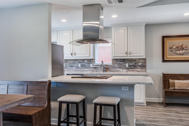 kitchen with freestanding refrigerator, light stone counters, island exhaust hood, and white cabinetry