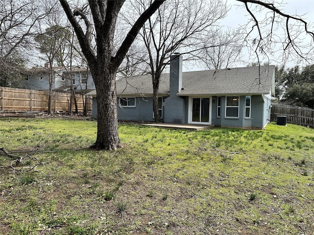 back of house featuring fence private yard, central air condition unit, brick siding, a lawn, and a chimney