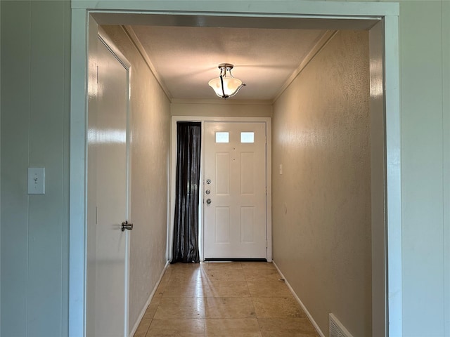 doorway with ornamental molding, light tile patterned flooring, a textured wall, and baseboards