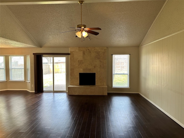 unfurnished living room with plenty of natural light, lofted ceiling, a fireplace, and dark wood finished floors