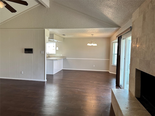 unfurnished living room with dark wood-style flooring, a fireplace, plenty of natural light, and ceiling fan with notable chandelier