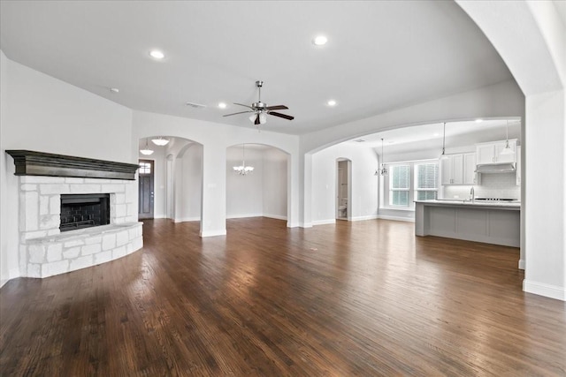 unfurnished living room with dark hardwood / wood-style flooring, sink, ceiling fan with notable chandelier, and a fireplace