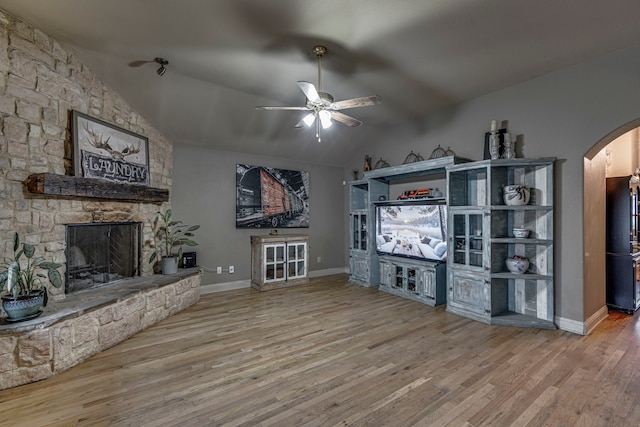 living room with lofted ceiling, a stone fireplace, wood-type flooring, and ceiling fan