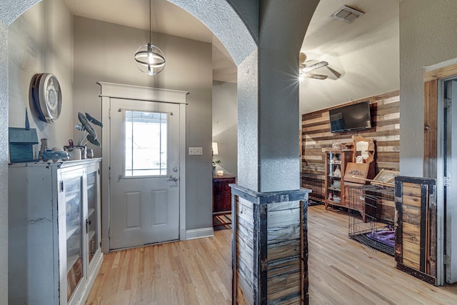 foyer featuring ceiling fan, light wood-type flooring, and wood walls