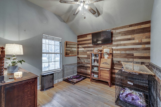 interior space featuring ceiling fan, lofted ceiling, wooden walls, and light hardwood / wood-style flooring