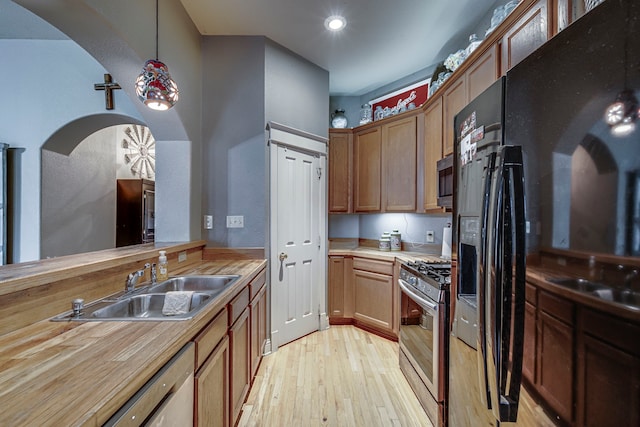 kitchen featuring sink, wooden counters, hanging light fixtures, light hardwood / wood-style flooring, and stainless steel appliances