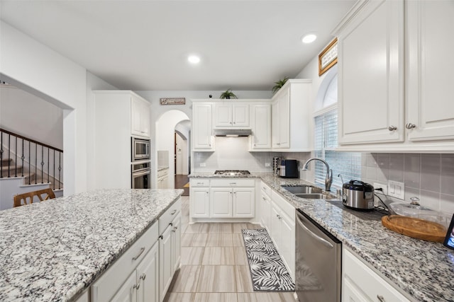 kitchen featuring appliances with stainless steel finishes, white cabinetry, sink, decorative backsplash, and light stone countertops