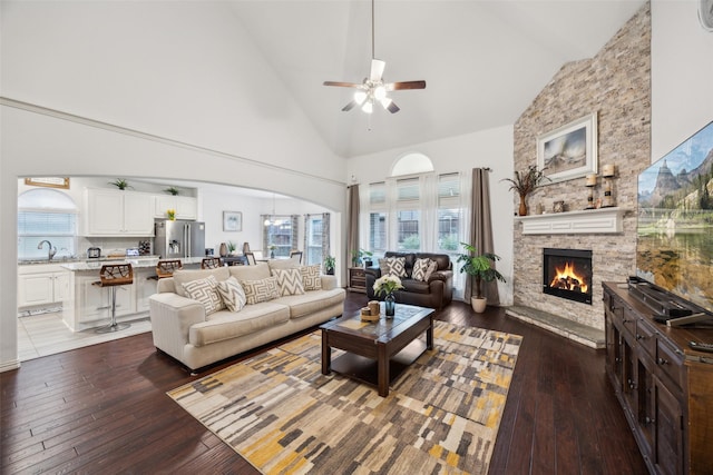 living room with a stone fireplace, dark hardwood / wood-style floors, sink, and high vaulted ceiling