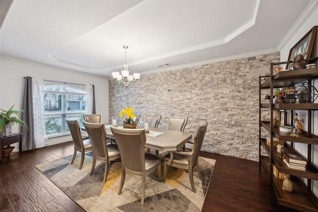 dining space with dark wood-type flooring, ornamental molding, a raised ceiling, and an inviting chandelier