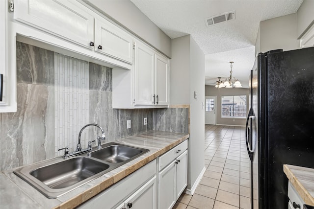 kitchen featuring black refrigerator, pendant lighting, sink, white cabinets, and light tile patterned floors