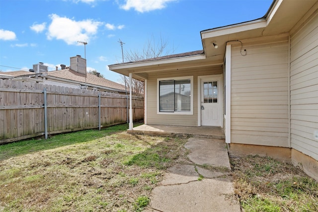 view of exterior entry with a yard, central AC unit, and a patio area