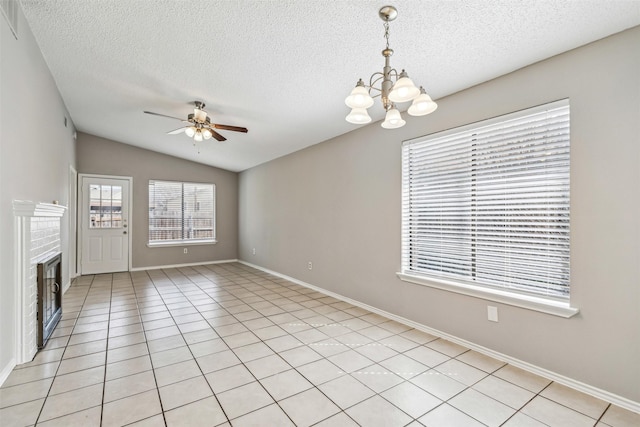 interior space featuring light tile patterned flooring, vaulted ceiling, a textured ceiling, a fireplace, and ceiling fan with notable chandelier