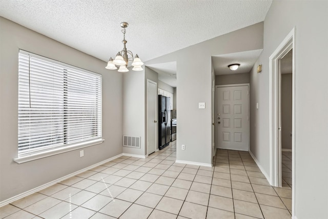 tiled empty room with an inviting chandelier and a textured ceiling