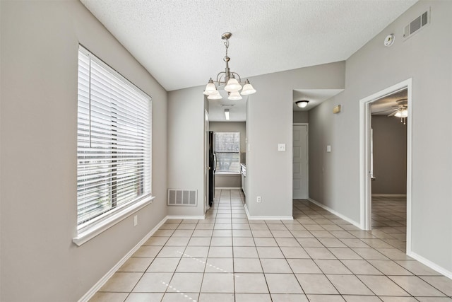 unfurnished dining area with light tile patterned flooring, ceiling fan with notable chandelier, and a textured ceiling