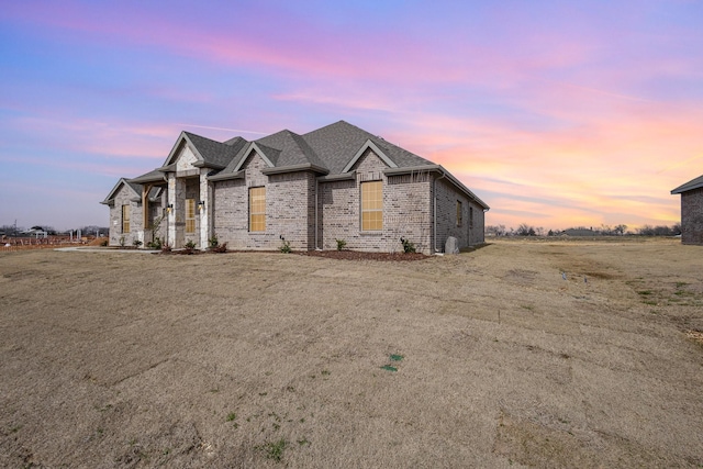 french country style house with roof with shingles and brick siding