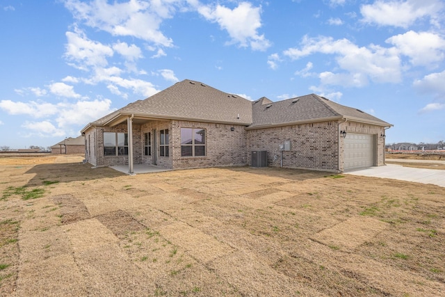 rear view of property with brick siding, a shingled roof, central AC unit, a garage, and driveway